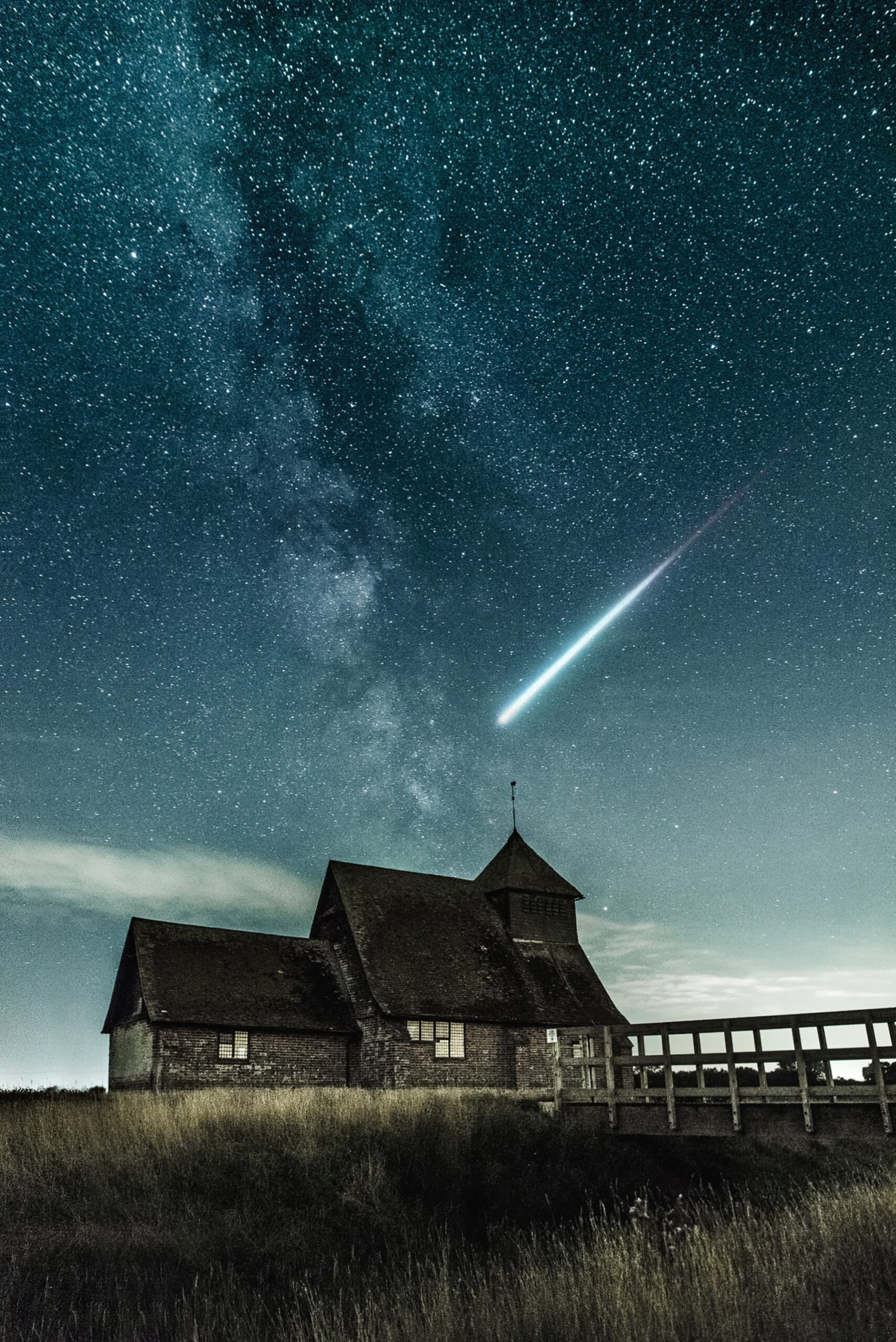 A comet shooting through a starry night sky above a house in a field