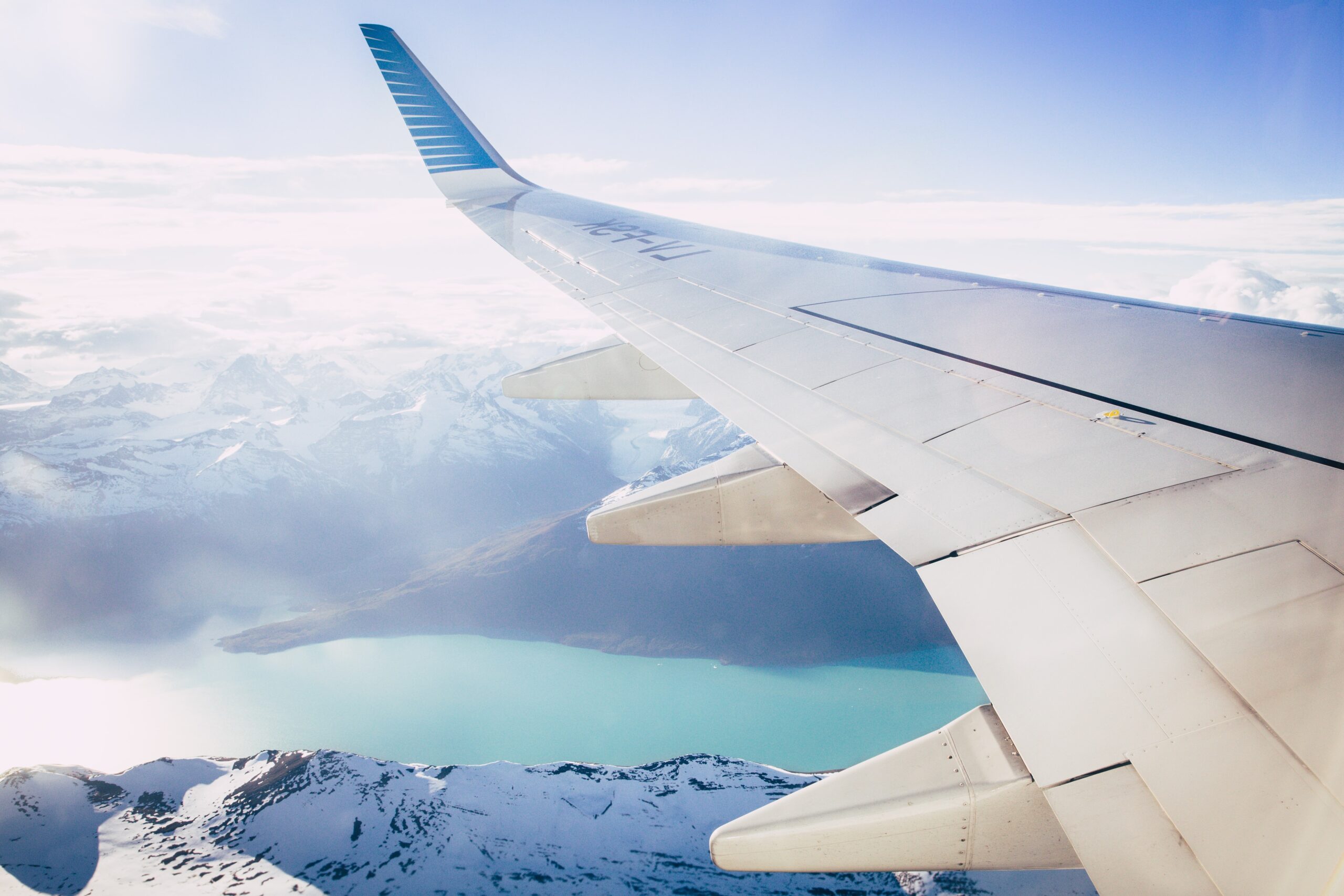 The wing of a plane flying above icy mountains