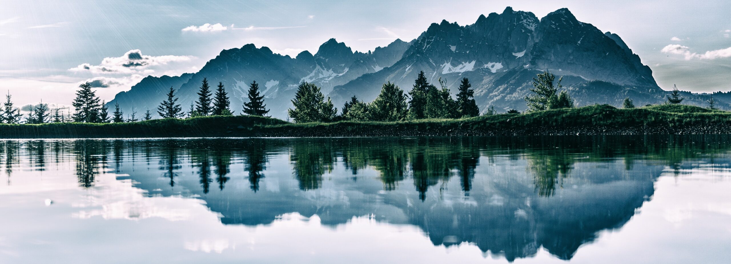 Green trees in front of a rocky mountain reflecting in the water of a lake