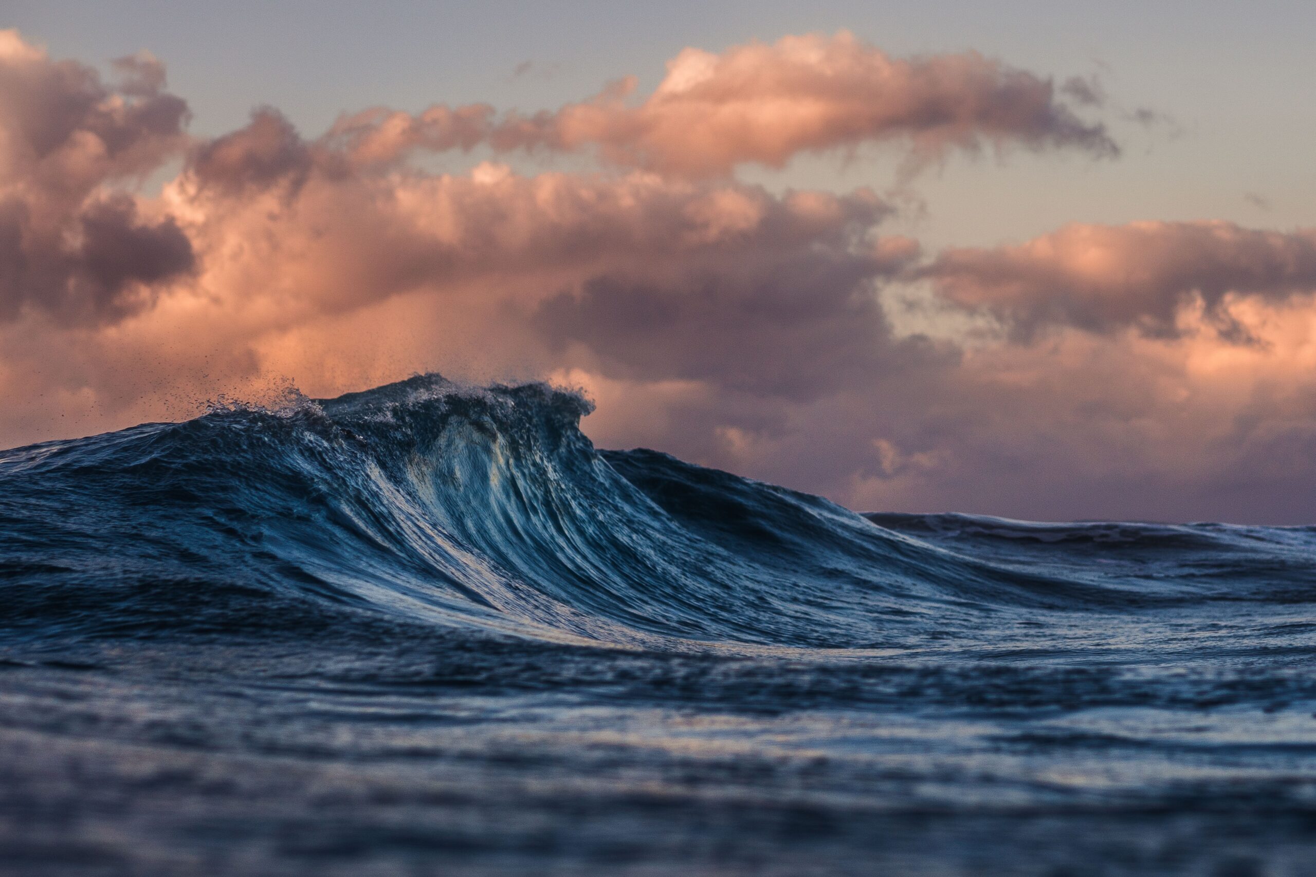 A close up of the peak of a wave that formed with sunset clouds behind it